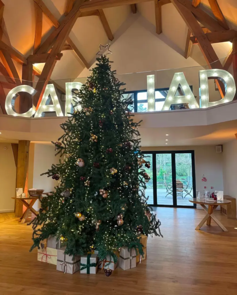 Christmas tree with wrapped presents in front of light-up letters at The Mill Barns