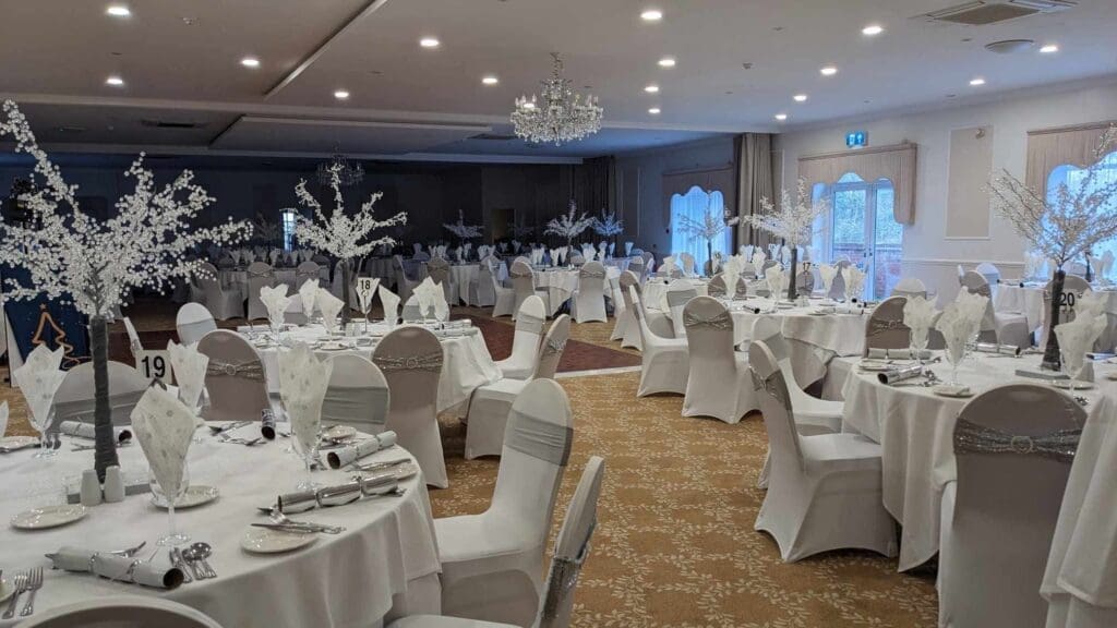 Function room set for a Christmas party night with white chair covers and tall white centrepieces