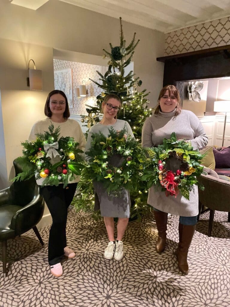 Three guests holding their finished Christmas wreaths at a wreath making class