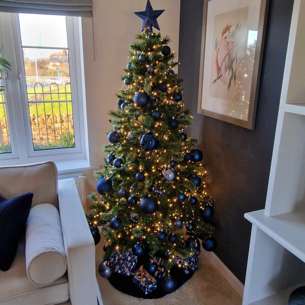 Christmas tree with navy and gold baubles and a star topper in a living room