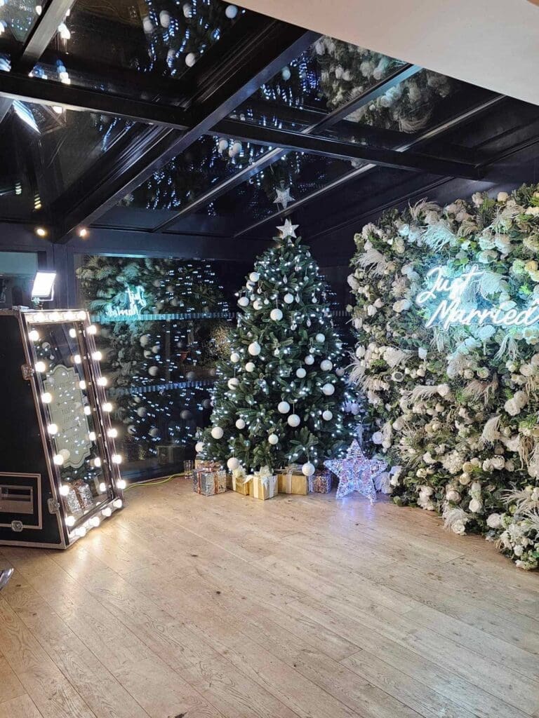 Christmas tree with warm lights between white flower walls and a light-up letter in a venue