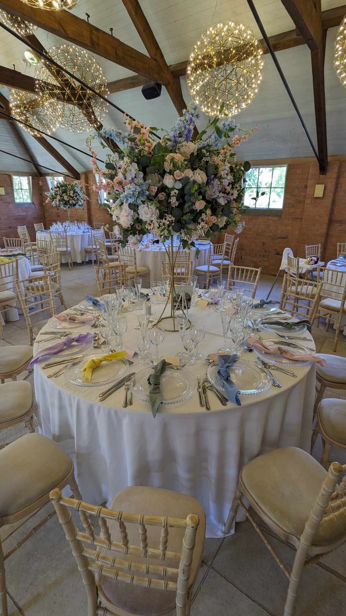 Round wedding table with a foliage centrepiece and gold chairs at Gorcott Hall