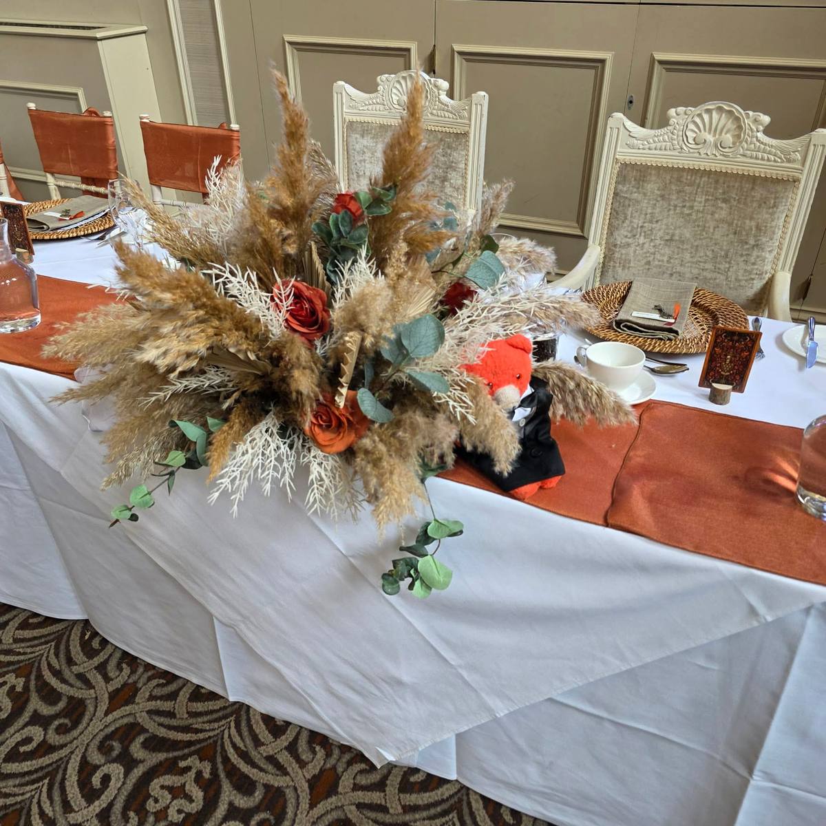 Pampas grass, eucalyptus and burnt orange roses on the top table at a Stanbrook Abbey wedding in St Anne's Hall